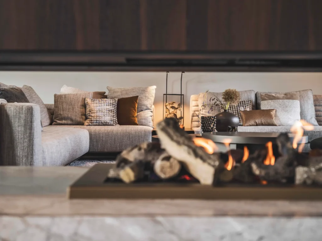 Sfeervol interieurontwerp door Eric Kant met een moderne doorkijkhaard op de voorgrond en een luxe zithoek met comfortabele banken en sierkussens op de achtergrond.