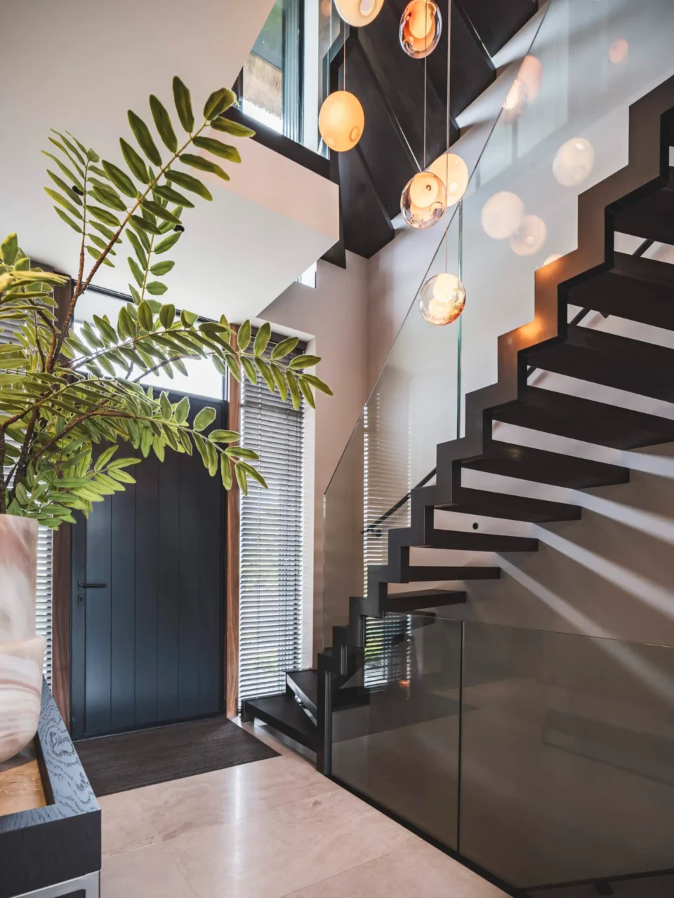 Exclusieve moderne trap ontworpen door Eric Kant, met zwarte treden, een glazen balustrade en opvallende Bocci hanglampen in een lichte vide.