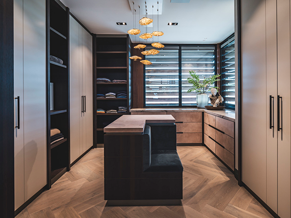 Exclusieve inloopkast ontworpen door Eric Kant, voorzien van maatwerk kasten, een centrale eilandmodule met zitgedeelte, een lichte visgraatvloer en sfeervolle hangverlichting.