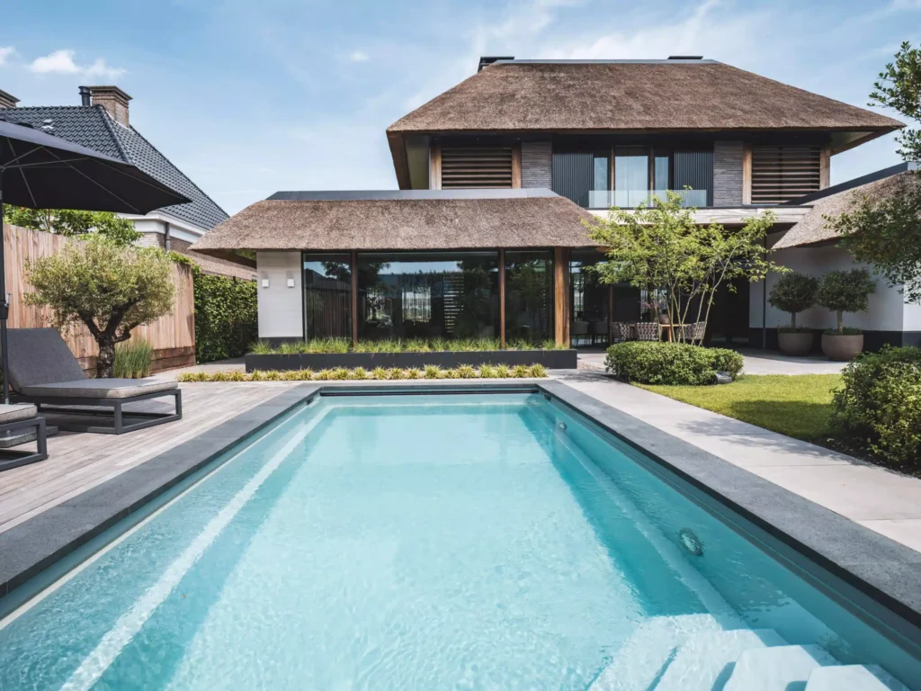 Exterieur van een luxe moderne villa door Eric Kant, met een groot strak zwembad, houten vlonderterras, ligbedden en een karakteristieke rieten kap.