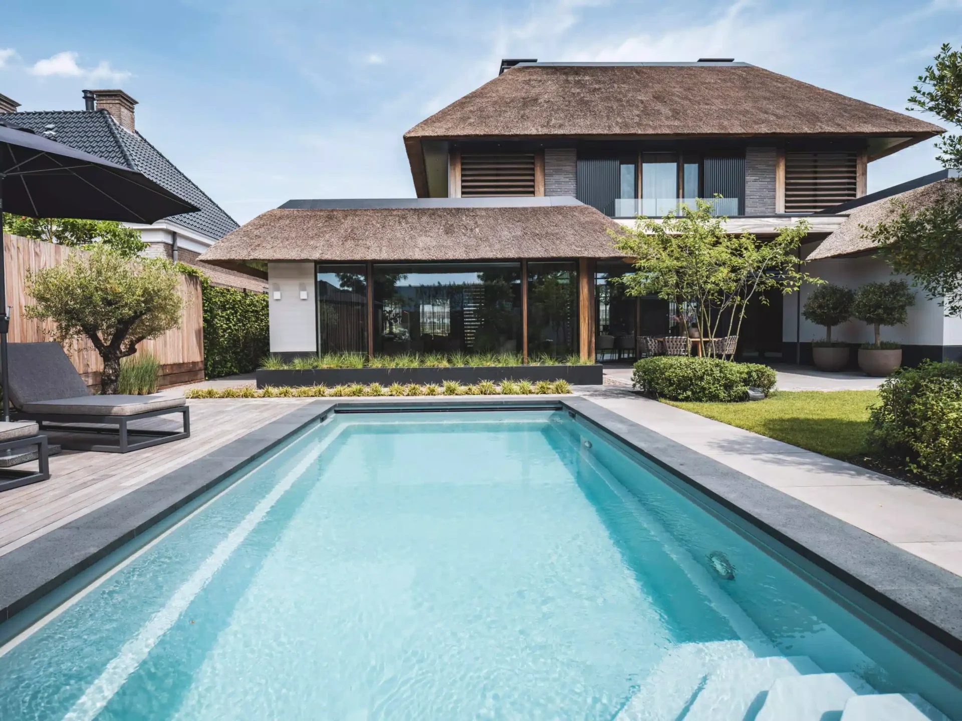 Exterieur van een luxe moderne villa door Eric Kant, met een groot strak zwembad, houten vlonderterras, ligbedden en een karakteristieke rieten kap.