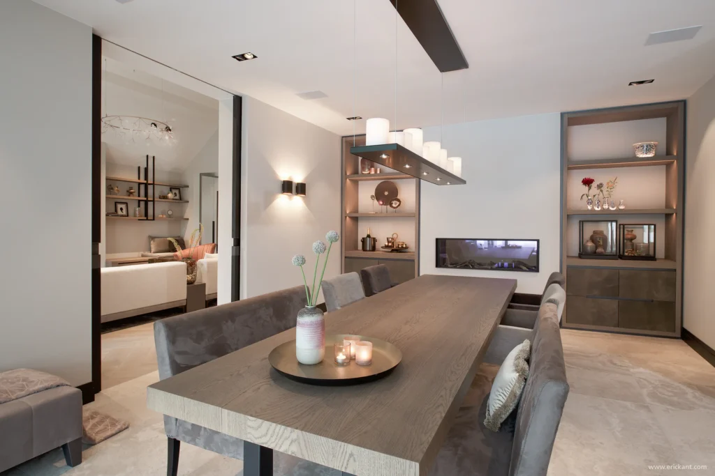 High-end eetkamer in de Manor Villa door ERIC KANT met een robuuste eikenhouten eettafel, fluwelen eetkamerbank en stoelen, een geïntegreerde gashaard en maatwerk nissen met verlichting.