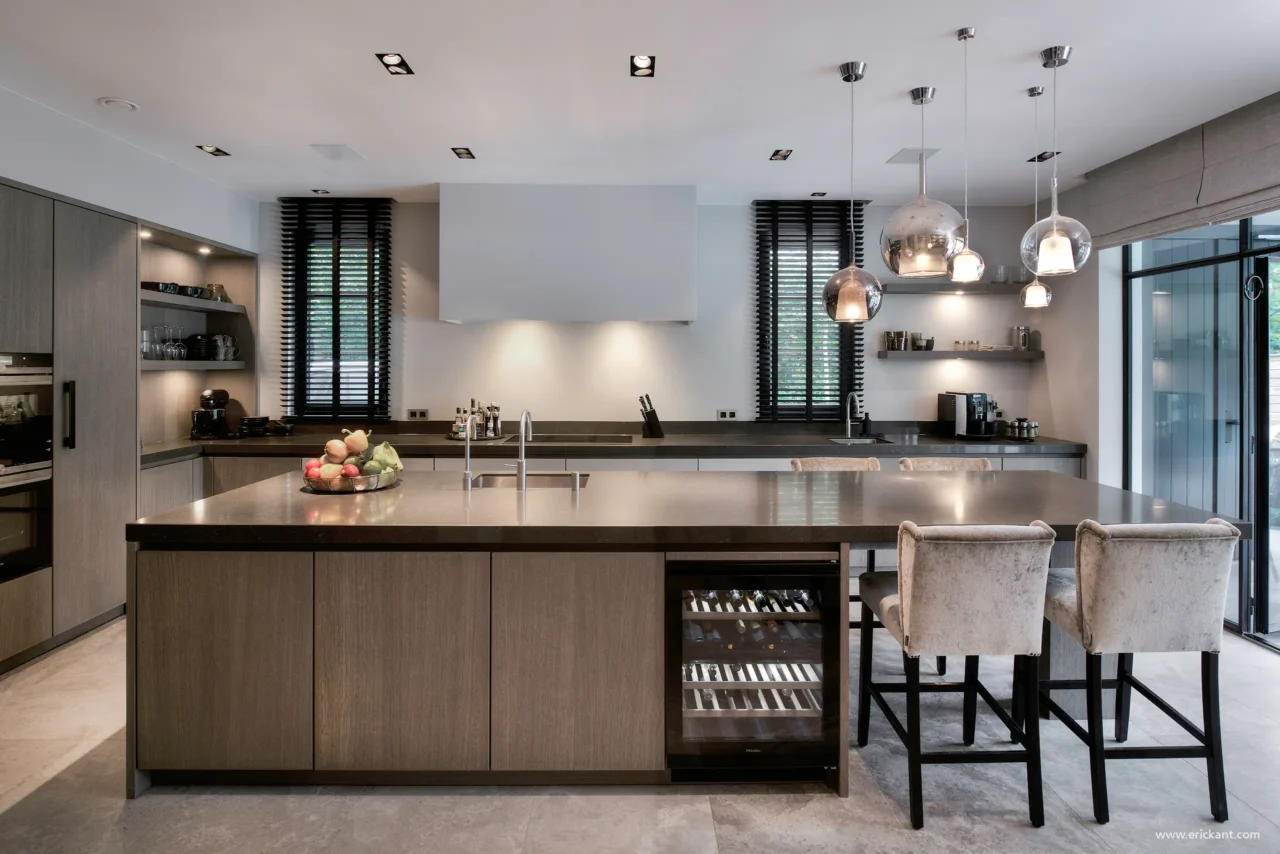 High-end keuken in de Modern Manor met een massief natuurstenen kookeiland, bronzen fronten, cognac lederen barkrukken, mondgeblazen hanglampen en een ingebouwde wijnklimaatkast door ERIC KANT.