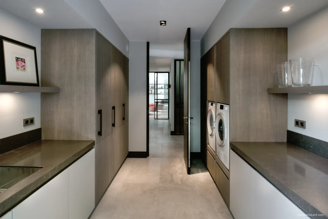 High-end bijkeuken en laundry in de Manor Villa door ERIC KANT met maatwerk kastenwanden in eikenhout, verhoogde wasmachine en droger, natuurstenen werkbladen en een strakke gietvloer.