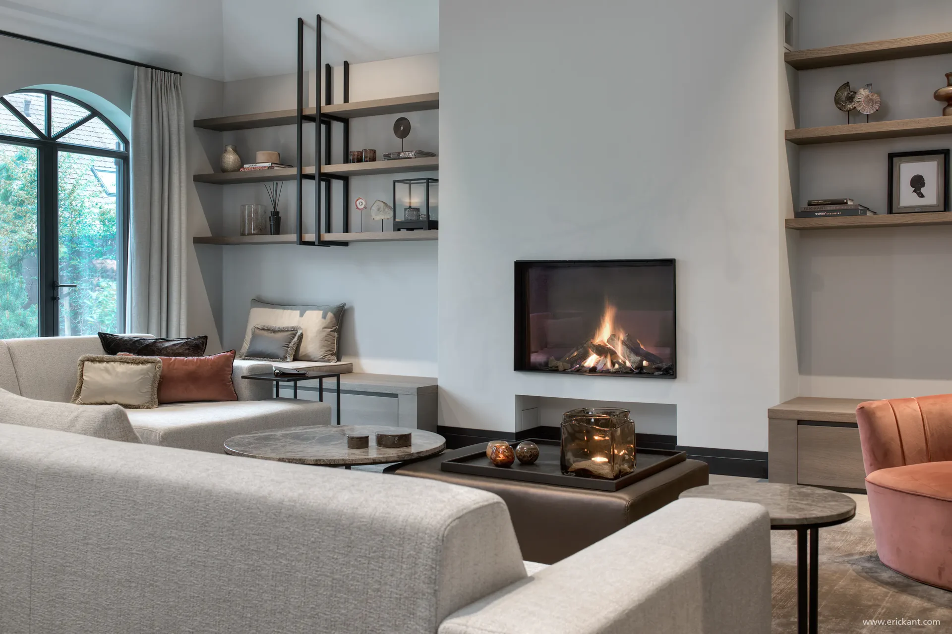 High-end interieur van de Manor Villa door ERIC KANT met een royale lichte zithoek, een moderne haard, maatwerk wandplanken, visgraatvloer en een indrukwekkend hoog plafond met designkroonluchter.