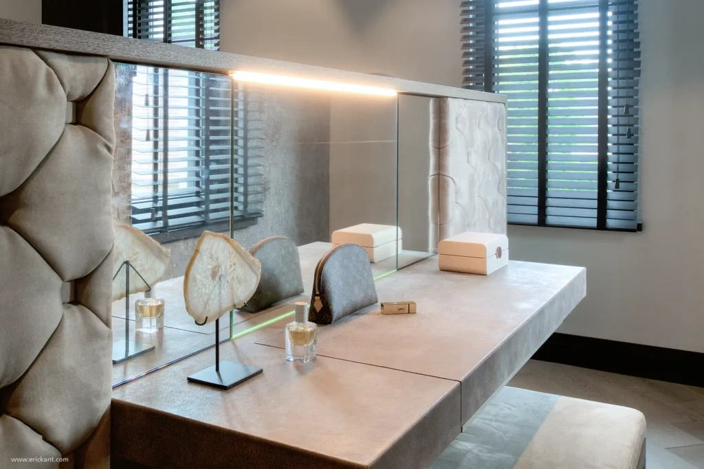 Detail van een luxe make-up tafel in de Manor Villa door ERIC KANT, bekleed met leder, met een geïntegreerde spiegel, verlichting en een gecapitonneerd hoofdbord van het bed op de achtergrond.