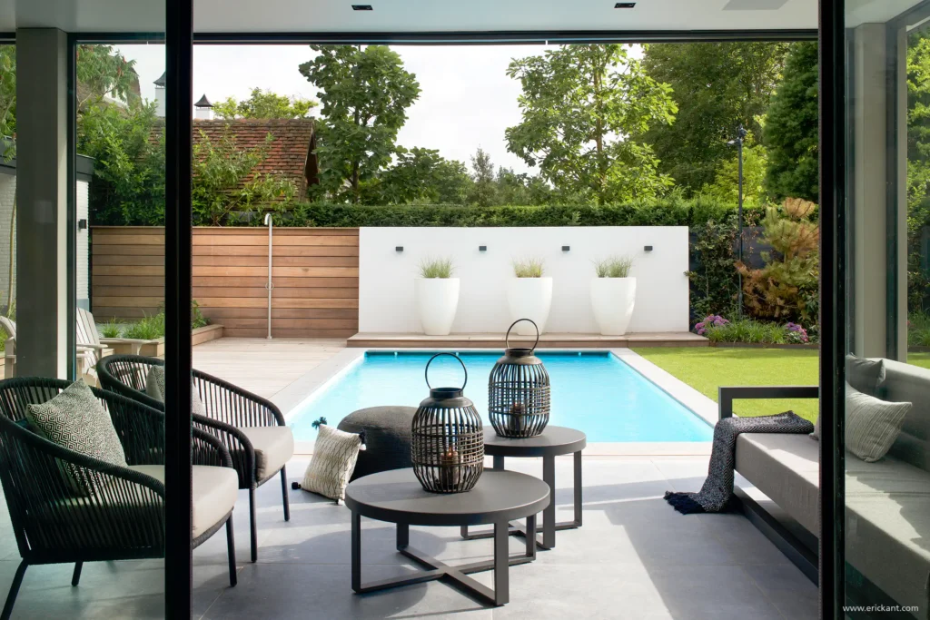 Zicht vanuit de living van de Manor Villa door ERIC KANT op het loungeterras en het strakke zwembad, met modern buitenmeubilair, grote witte plantenbakken en een houten privacywand.