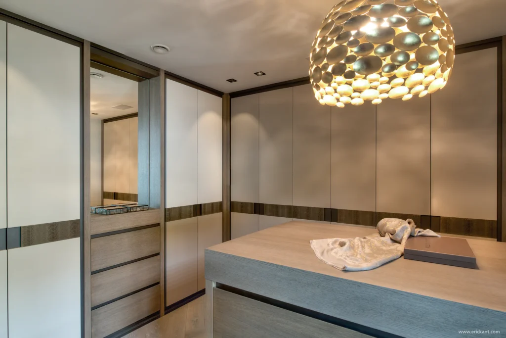 High-end inloopkast in de Manor Villa door ERIC KANT met kamerhoge maatwerk kasten, lederen details, een centraal lade-eiland en een goudkleurige designlamp.
