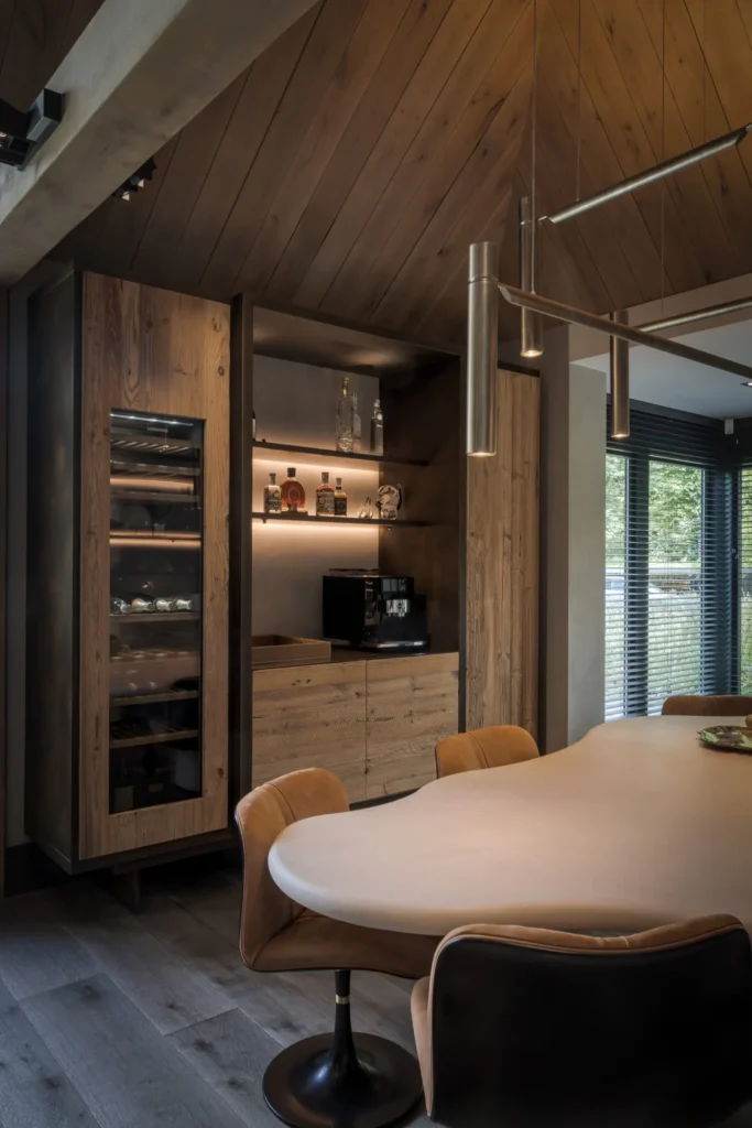 Exclusieve koffiecorner en wijnklimaatkast ontworpen door Eric Kant, met robuust houten kastenwand, sfeervolle led-verlichting en een organische eettafel op de voorgrond.
