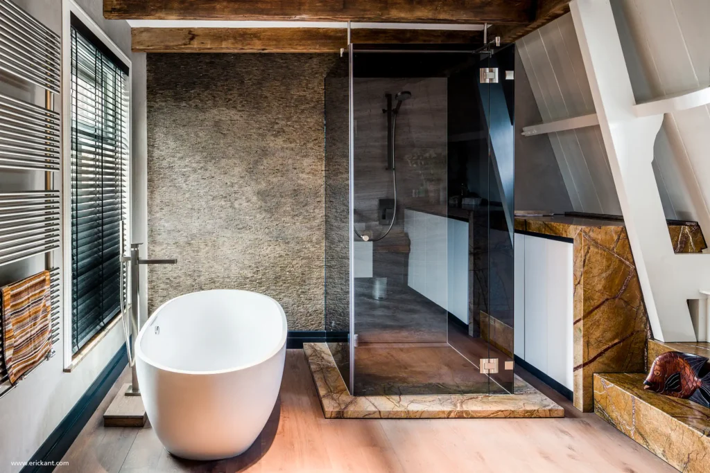 High-end badkamer in Riga met vrijstaand eivormig bad, glazen inloopdouche en natuurstenen accenten onder een schuin dak door ERIC KANT.