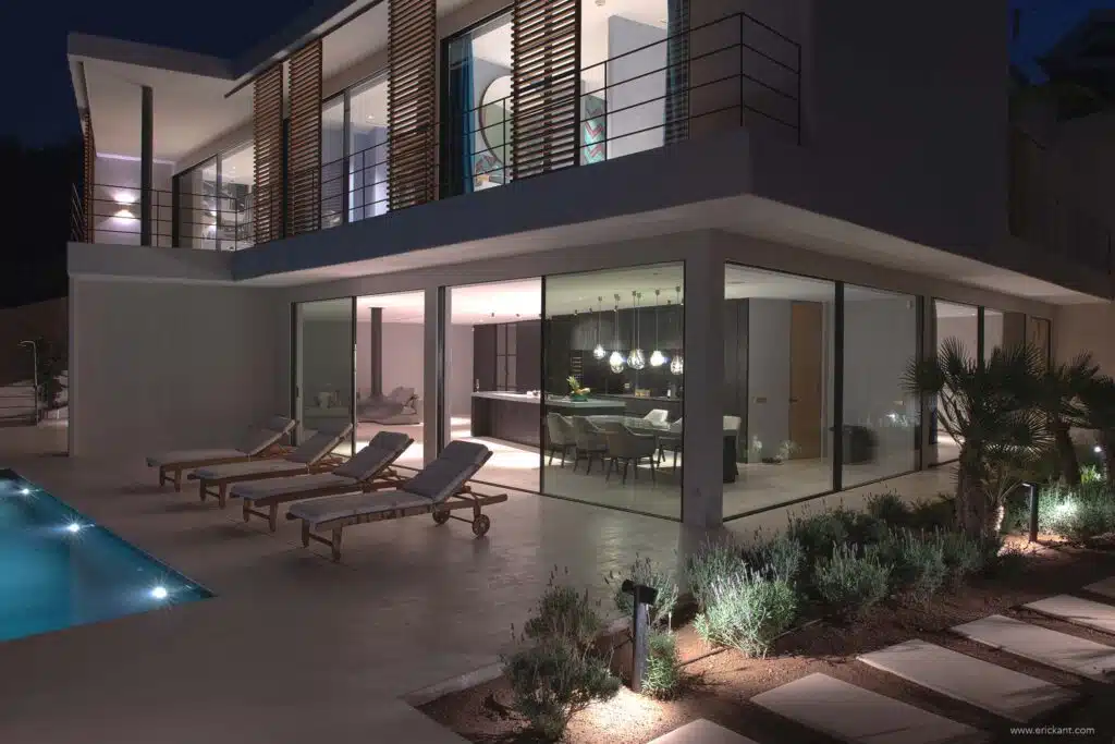 Luxe moderne villa in Ibiza bij nacht met verlicht zwembad, design buitenmeubilair en glazen gevel door ERIC KANT.