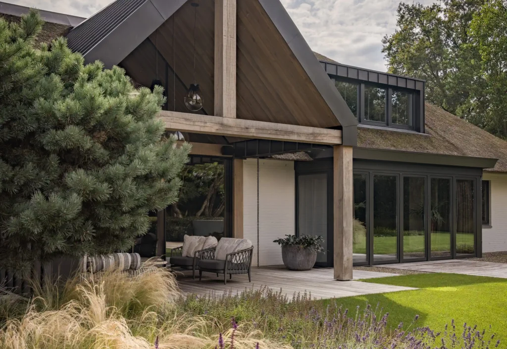Exterieur van een luxe lodge ontworpen door Eric Kant, met een karakteristieke rieten kap, robuuste eikenhouten balken, een houten vlonderterras en grote glazen puien.