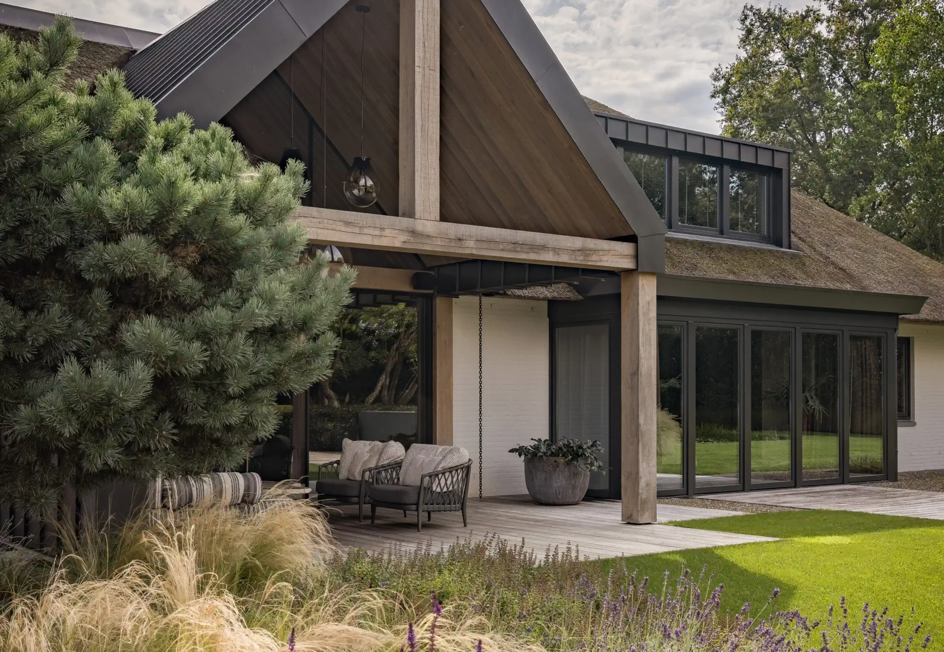 Exterieur van een luxe lodge ontworpen door Eric Kant, met een karakteristieke rieten kap, robuuste eikenhouten balken, een houten vlonderterras en grote glazen puien.