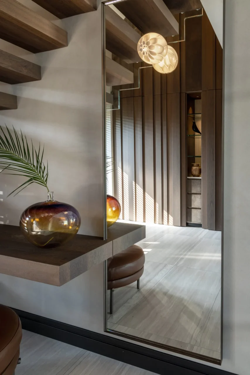 Detail van de hal in Villa Essenza door ERIC KANT met een grote passpiegel die de zwevende trap, een houten wandpaneel en een glazen designvaas reflecteert.
