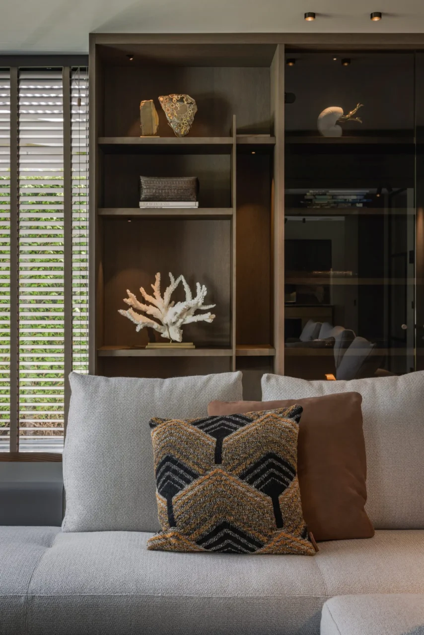 Detail van een maatwerk wandkast in Villa Essenza door ERIC KANT met verlichte nissen, decoratieve objecten zoals koraal en fossielen, en een comfortabele bank met luxe kussens.