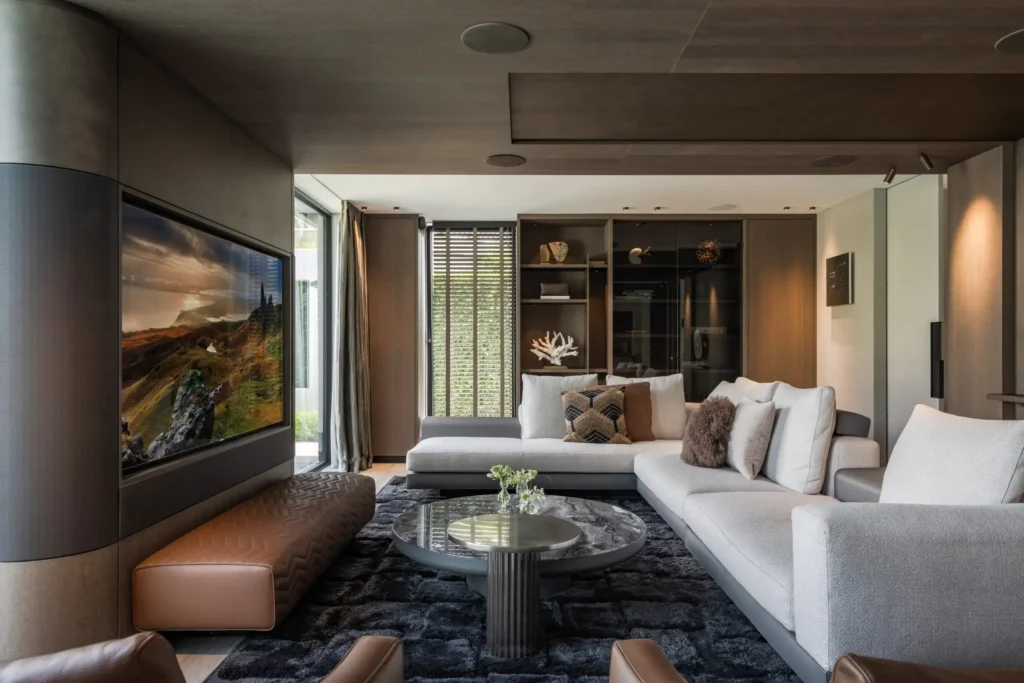 Interieur van de woonkamer in Villa Essenza door ERIC KANT met een grote geïntegreerde tv-wand, een luxe hoekbank, marmeren salontafels en een hoogpolig donker tapijt.