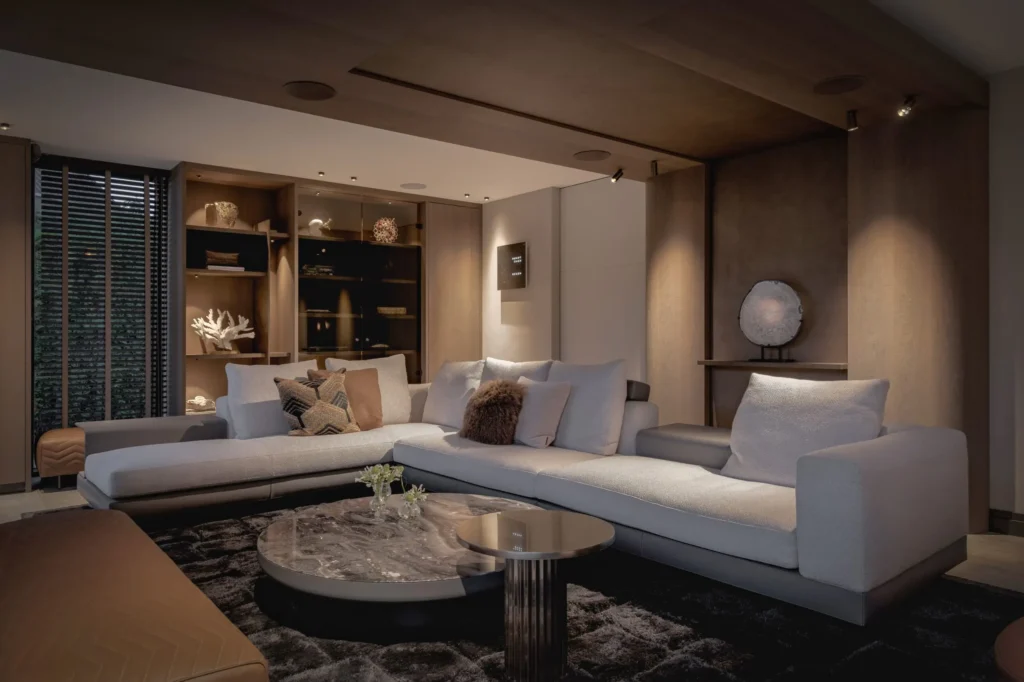 Luxe woonkamer in Villa Essenza door ERIC KANT bij avondlicht, met een verlichte maatwerkkast, een comfortabele hoekbank, marmeren tafels en een warm houten plafondontwerp