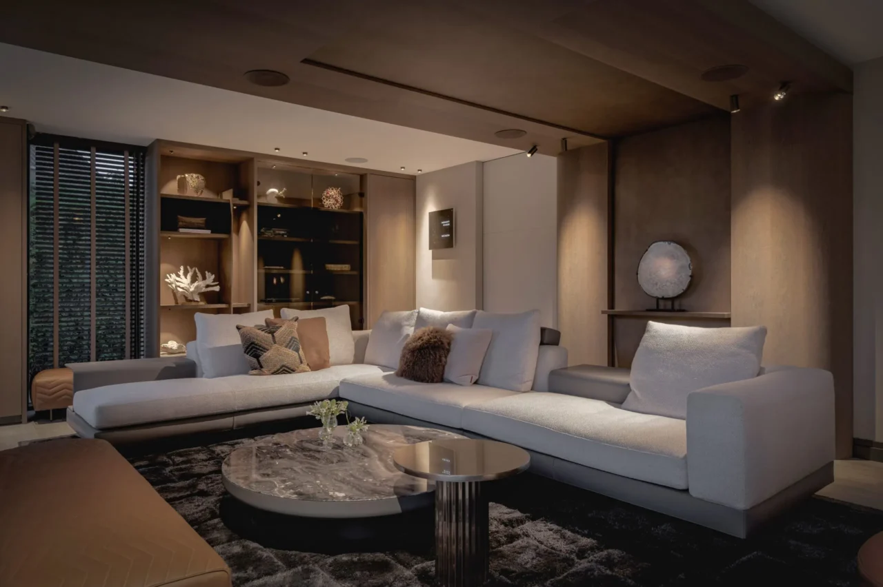 Luxe woonkamer in Villa Essenza door ERIC KANT bij avondlicht, met een verlichte maatwerkkast, een comfortabele hoekbank, marmeren tafels en een warm houten plafondontwerp