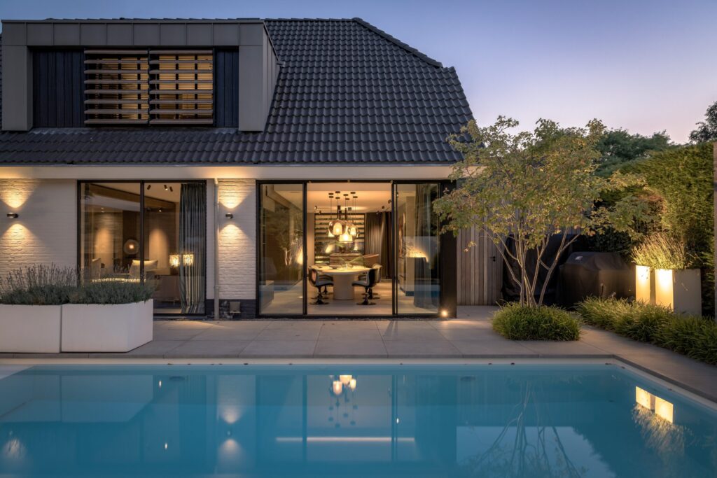 Achteraanzicht van Villa Essenza door ERIC KANT bij schemering, met een verlicht zwembad, een strak terras, grote glazen puien en zicht op het luxe interieur.