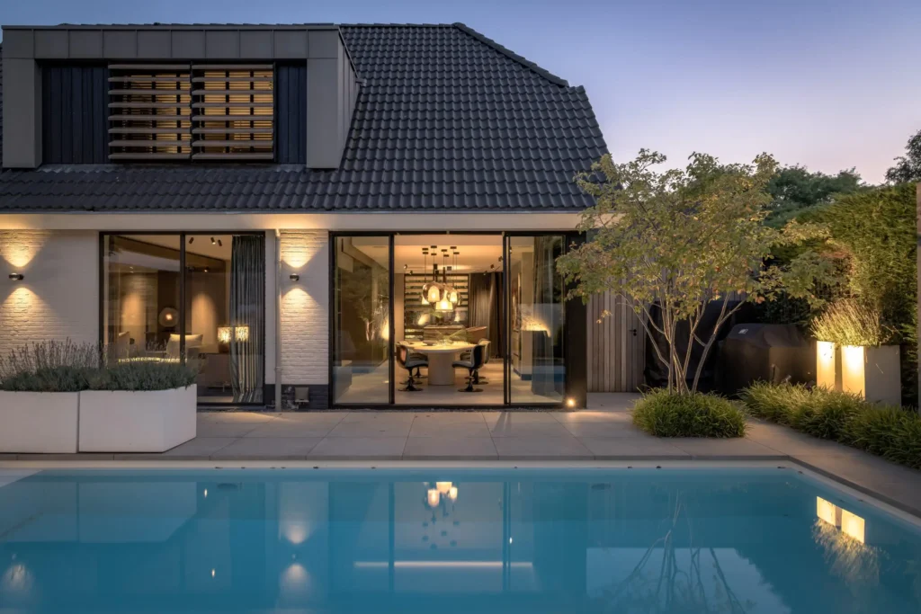 Achteraanzicht van Villa Essenza door ERIC KANT bij schemering, met een verlicht zwembad, een strak terras, grote glazen puien en zicht op het luxe interieur.
