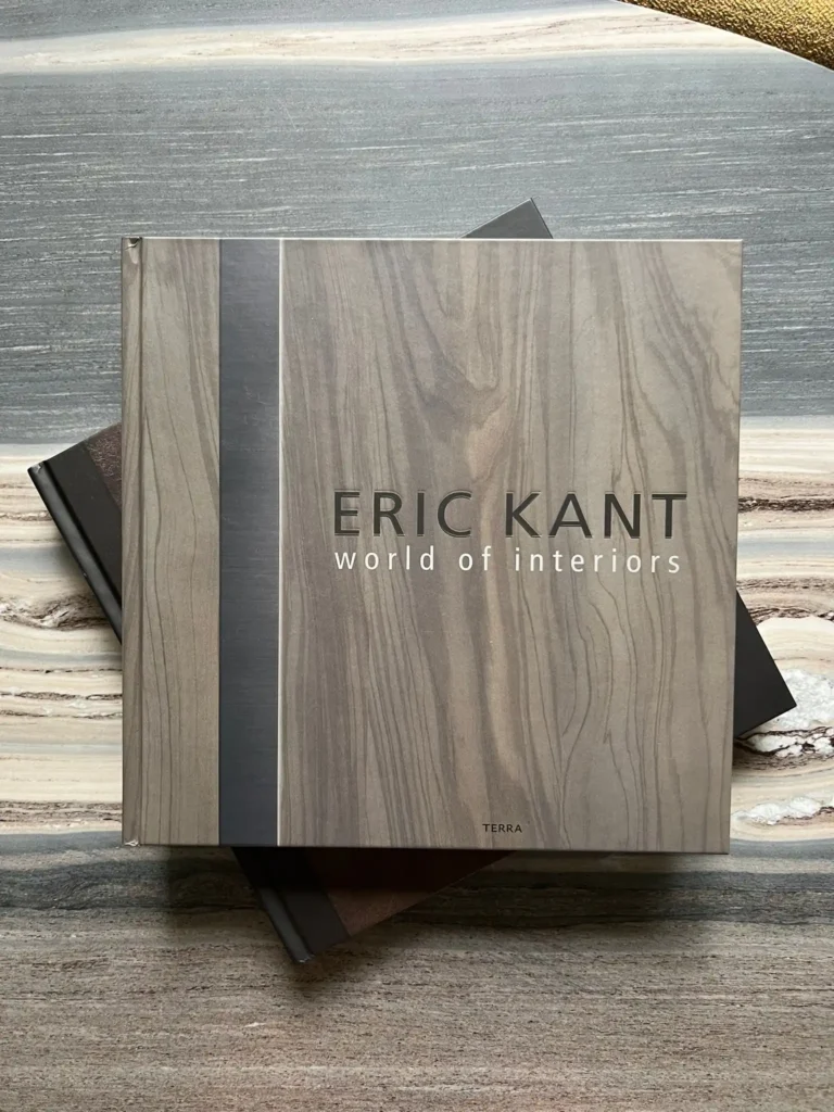 Een bovenaanzicht van het luxe koffietafelboek 'ERIC KANT world of interiors' door uitgeverij Terra, met een cover in een verfijnde houtstructuur, liggend op een exclusief marmeren blad.