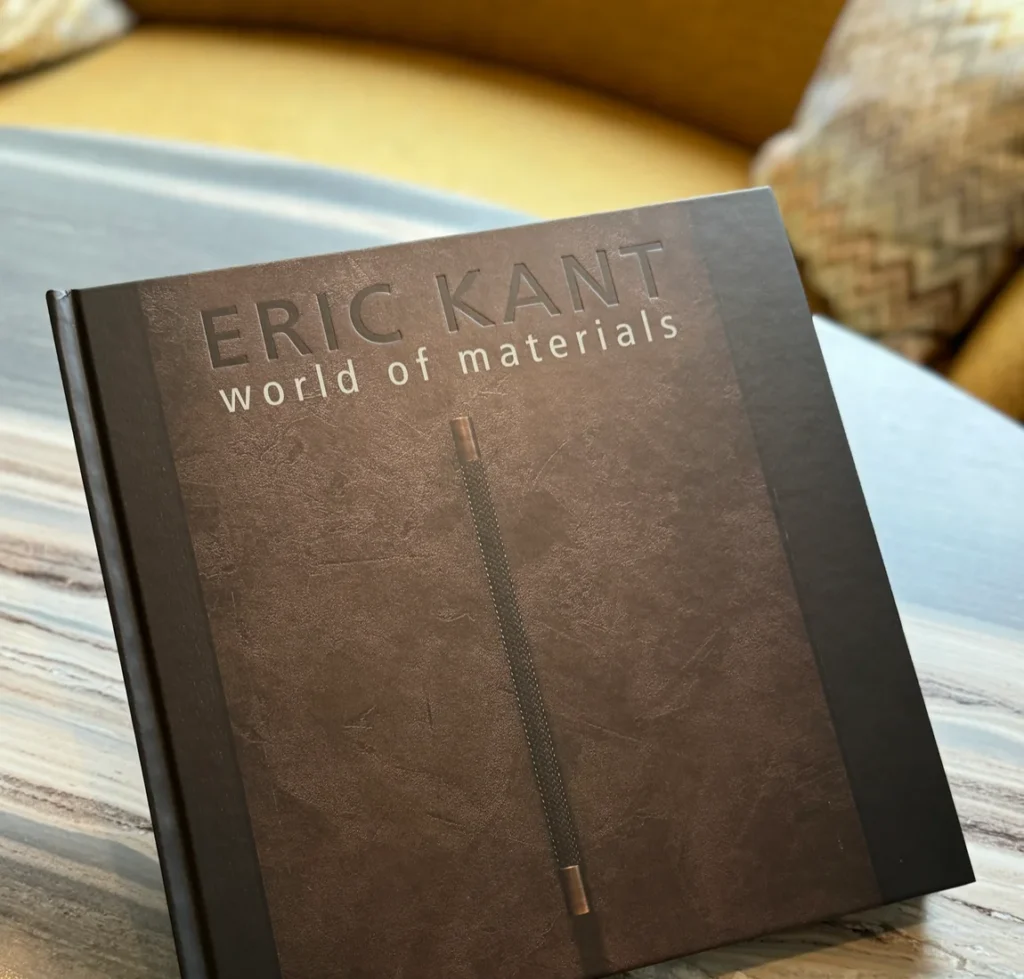 Het exclusieve interieurboek 'World of Materials' van Eric Kant, met een donkere gestructureerde kaft en koperen details, liggend op een tafel.