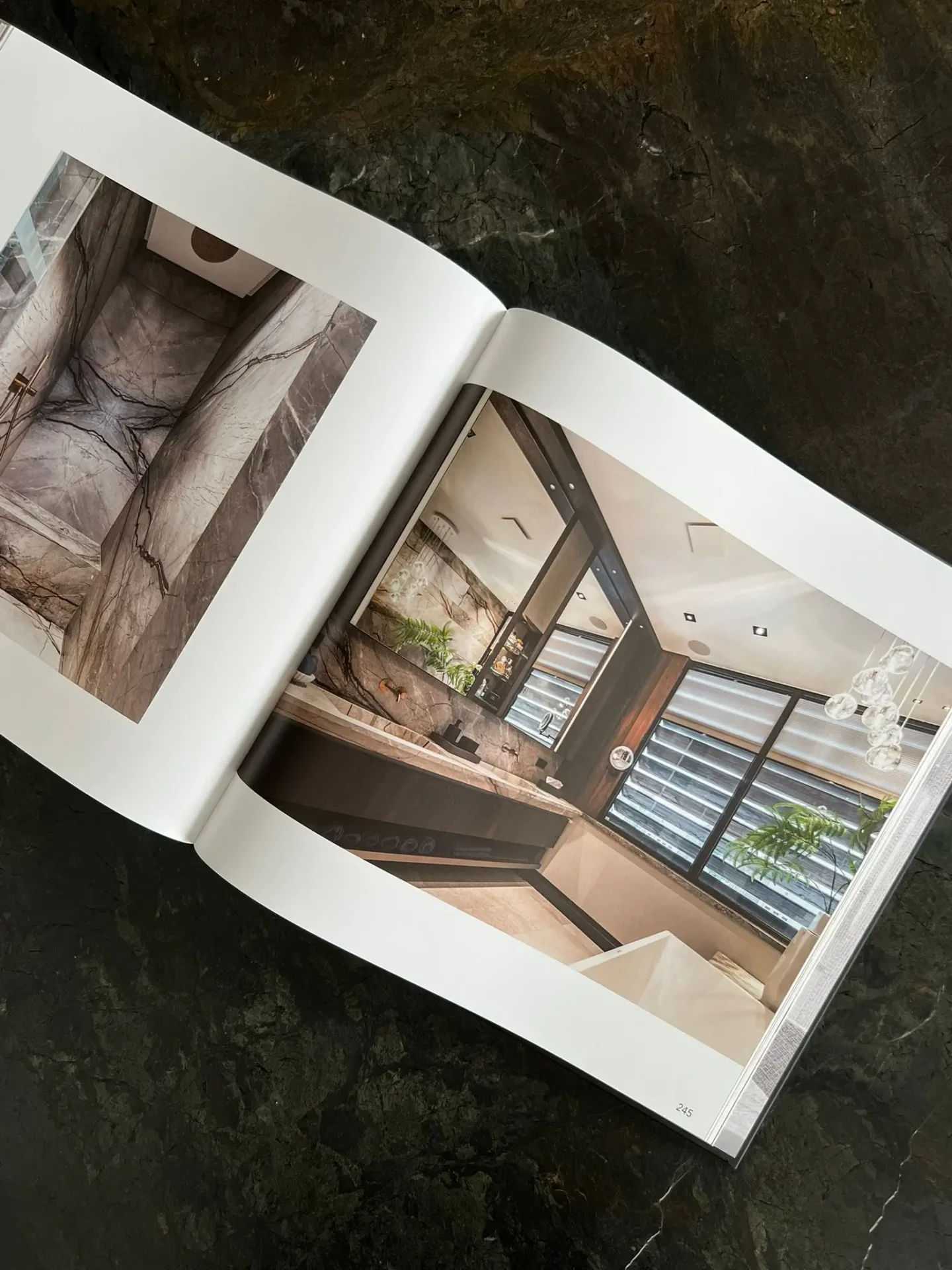 Een opengeslagen exemplaar van het boek van ERIC KANT op een donker marmeren blad, met pagina's die een luxe badkamer tonen met bookmatch natuursteen, een zwevend wastafelmeubel en een vrijstaand bad.