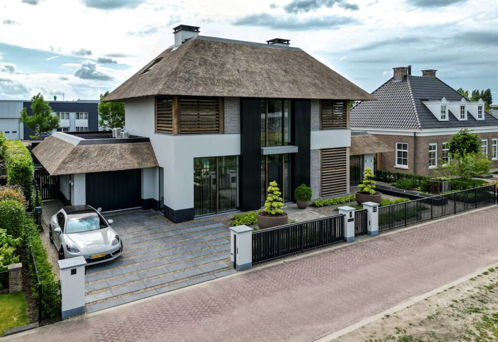 Vooraanzicht van een luxe moderne villa ontworpen door ERIC KANT, met een rieten dak, grote glaspartijen, een terras en een symmetrische gevel