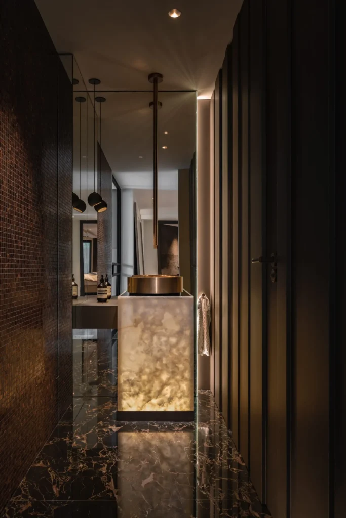 High-end toiletinterieur in de Metropolitan Luxury villa met een verlicht wastafelmeubel van onyx, een bronzen waskom, marmeren vloer en wanden van mozaïek door ERIC KANT.