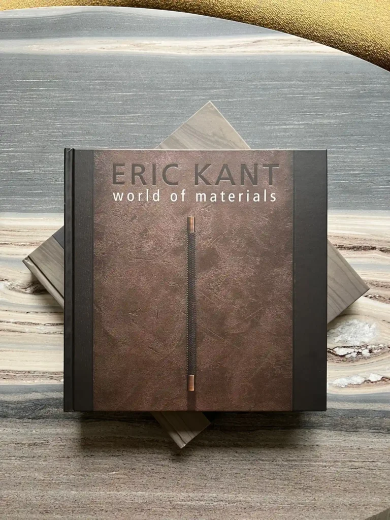 Een bovenaanzicht van het luxe koffietafelboek 'ERIC KANT world of materials', met een textured bruine cover en koperen details, liggend op een exclusief marmeren blad.