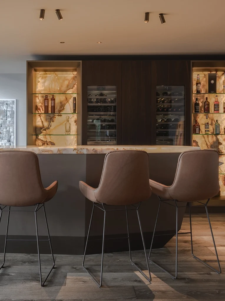 Luxe thuisbar op maat ontworpen door Eric Kant, met verlichte onyx panelen, geïntegreerde wijnklimaatkasten, lederen barkrukken en exclusieve Modular plafondspots.